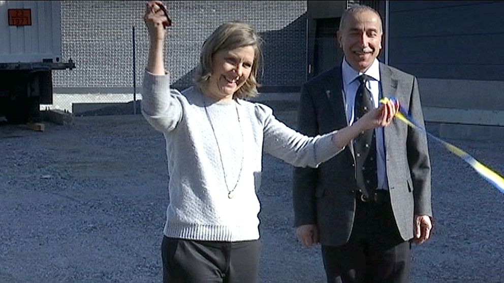 Kvinna (miljöminister) med sax i ena handen (höjd) har just klippt av blågult band. Man med slips står bredvid.