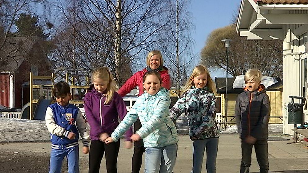 fem barn och en vuxen i en dansrörelse på skolgård