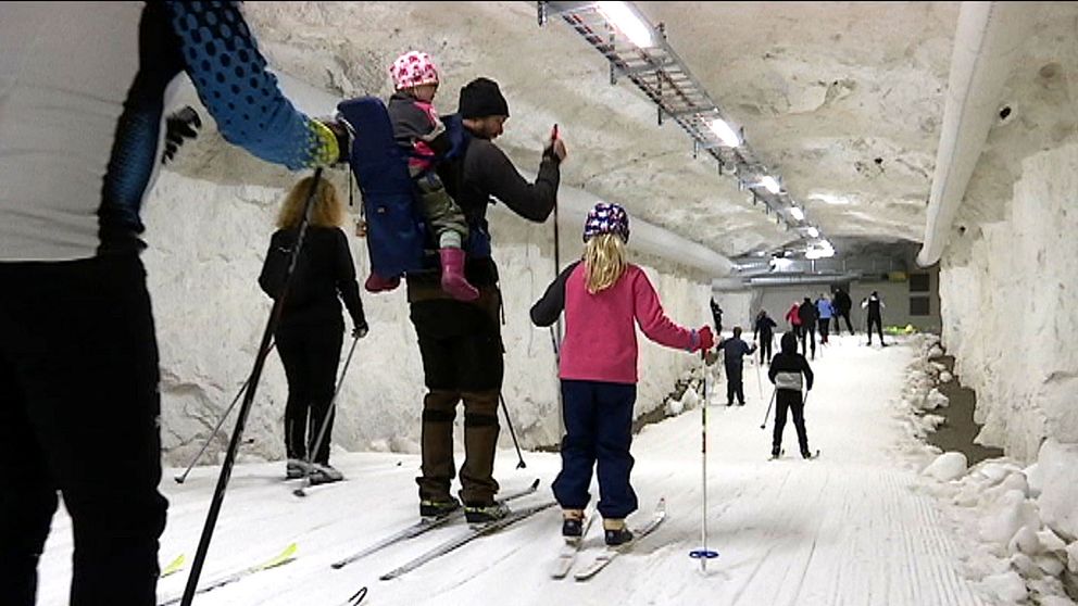 Vuxna och barn åker skidor inne i en tunnel med snö och skidspår.