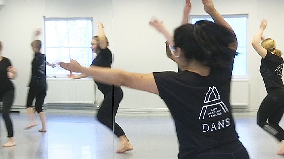 Fem ungdomar dansar iklädda svarta kläder. På personen i förgrunden syns AlmaAkademins logotyp på ryggen.