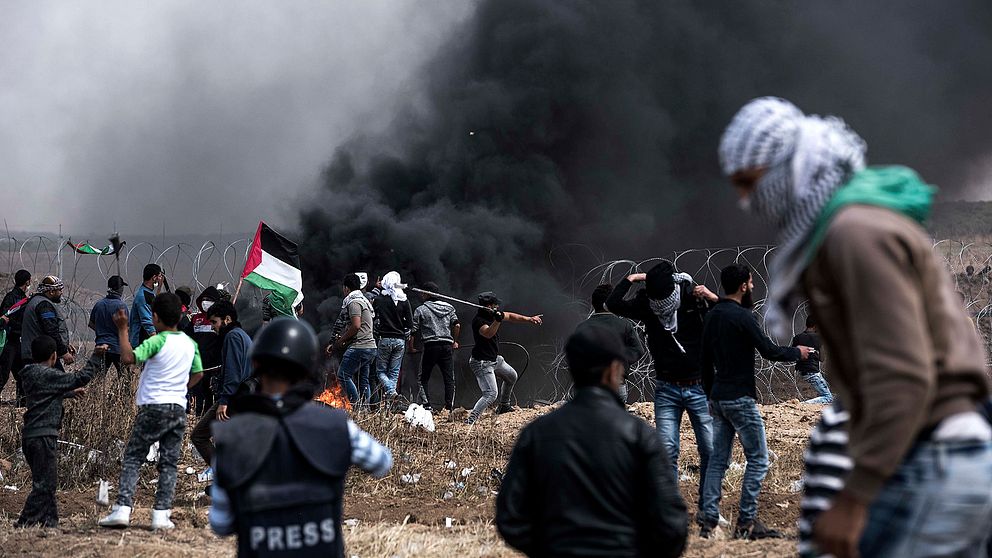 Tjock svart rök stiger, palestinska flaggor viftas och maskerade män som protesterar i Gaza.
