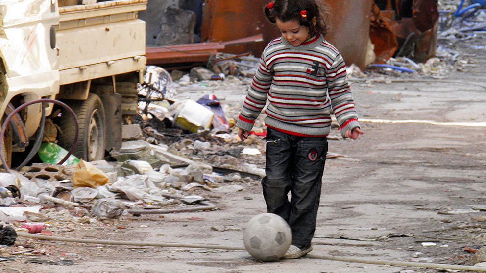En flicka leker med en fotboll på en av de sönderbombade gatorna i centrala Homs.