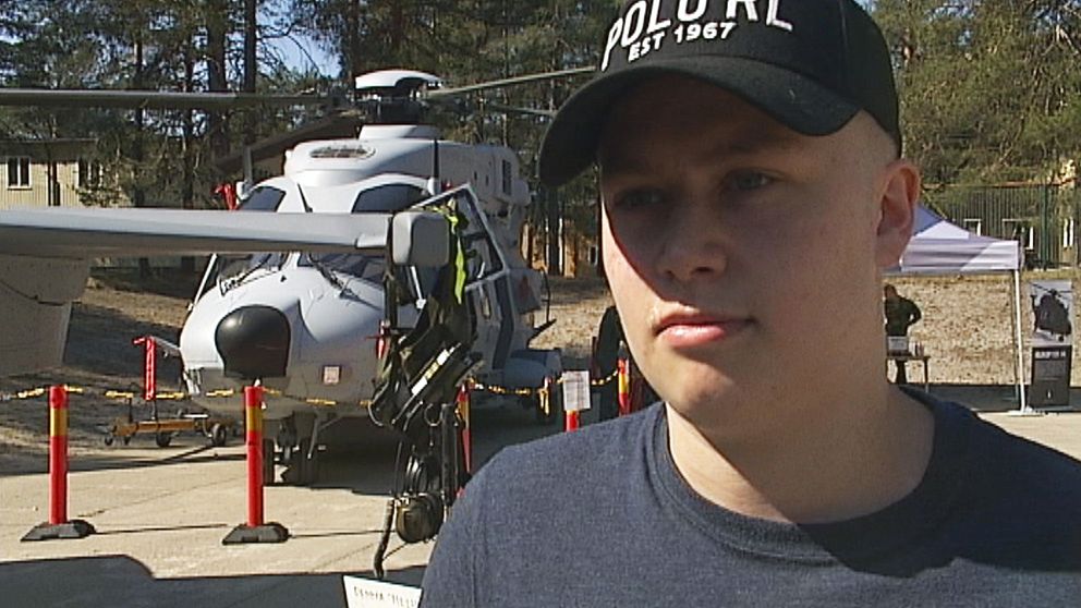 En ung man med keps intervjuas framför en helikopter.