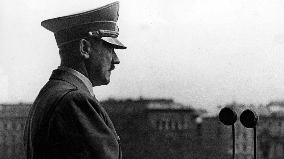 Adolf Hitler står på en balkong och tittar ut.