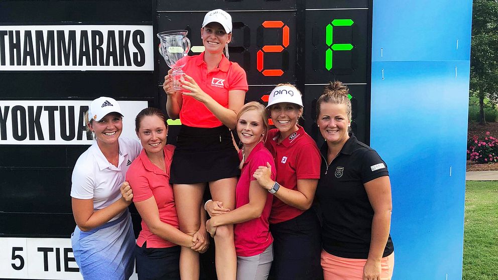 Golfaren Jenny Haglund, med en buckla av glas i händerna, lyfts upp av fem andra kvinnor framför en scoreboard.