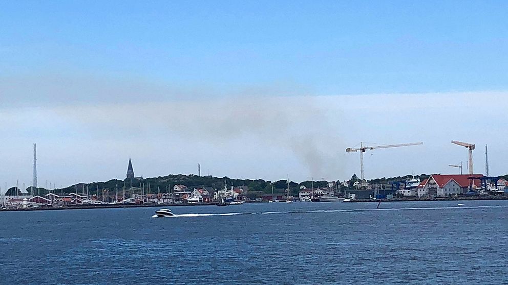 Bild med båtar, kranar och byggnade i Öckerö hamn och rökutveckling från avfallsanläggningen