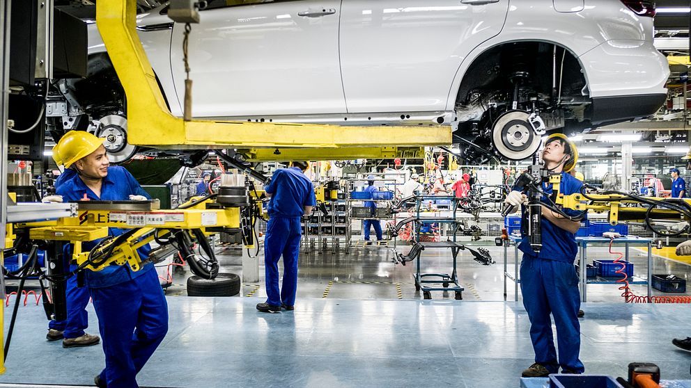 Fabriksarbetare i blå kläder monterar bilar i en fabrik.