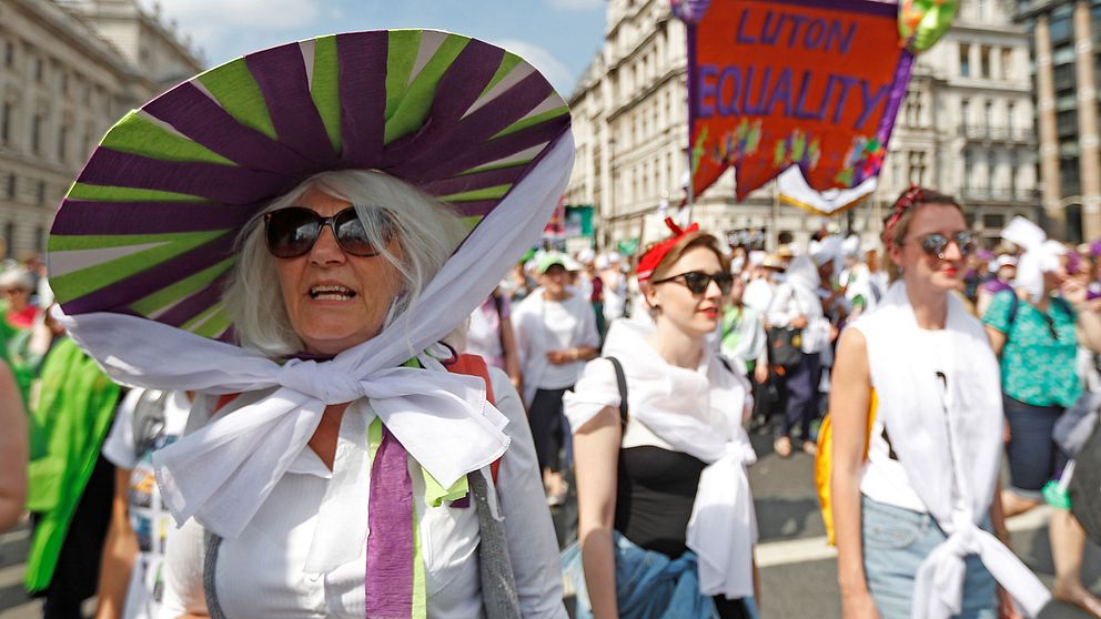 En kvinna med hatt i suffragetternas färger marscherar på Londons gator.