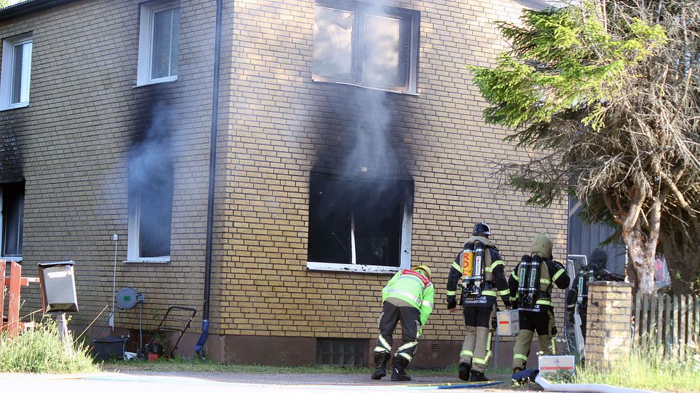 brandpersonal utanför större tegelhus, ryker ur fönstren