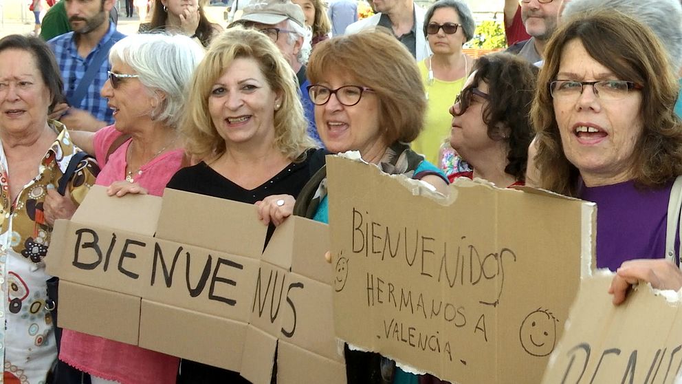 I Valencias hamn har folk samlats för att ta emot fartyget Aquarius. En grupp kvinnor tillverkar skyltar där det står ”Välkomna!”.