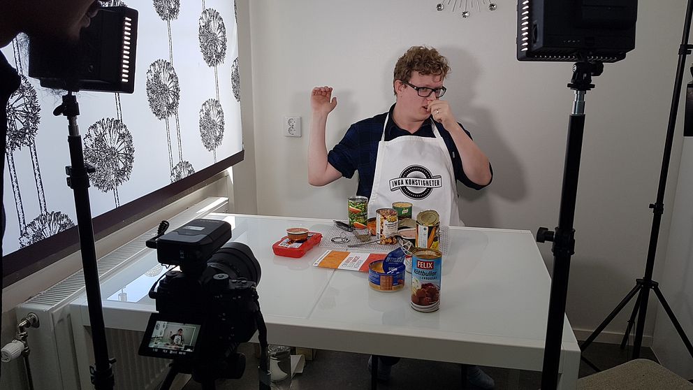 Youtubern Figgehn sitter vid ett bord med olika konserver framför sig.