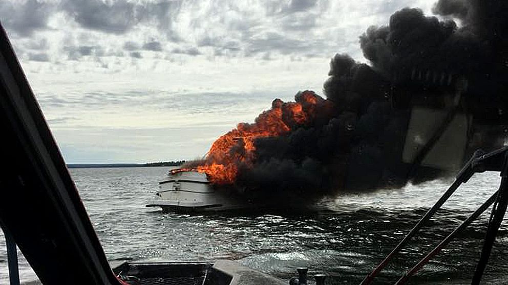 Kraftig rökutveckling och brandlågor slår ut från en vit båt.