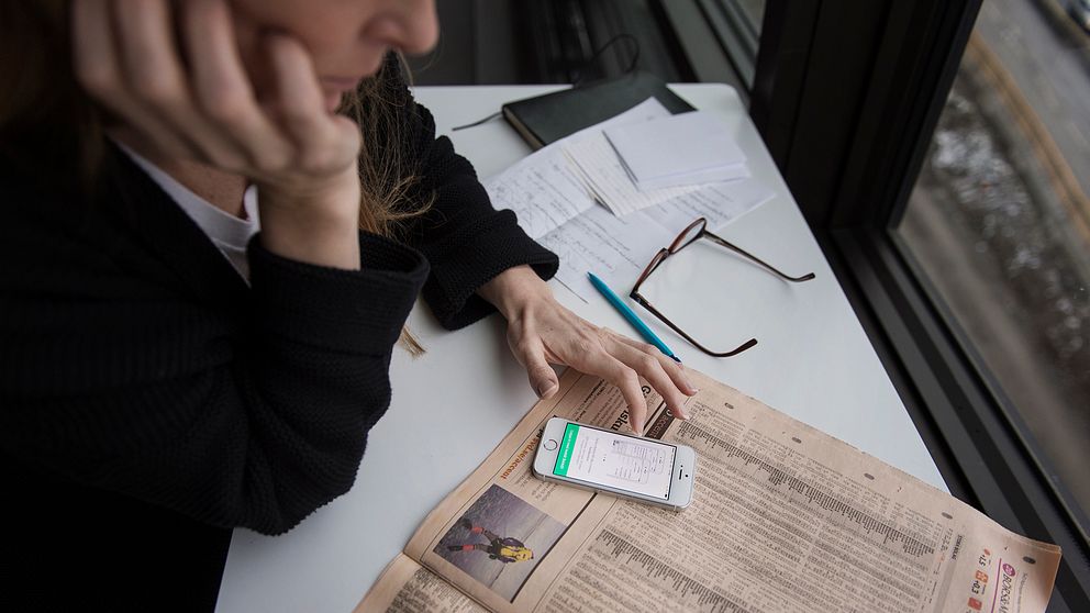 Kvinna som sitter med en tidning och en app.
