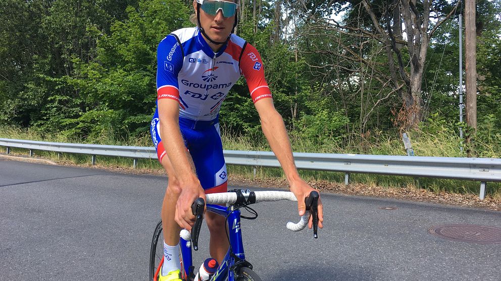 Tävlingsklädd cyklist i blått, vitt och rött på blå racercykel