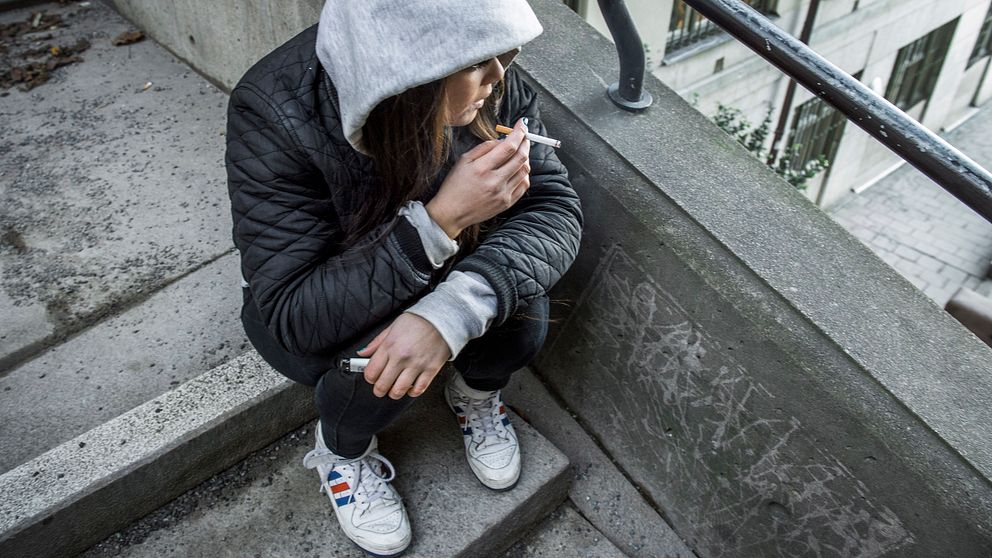 tonårstjej sitter på en trappa och röker en cigarett.