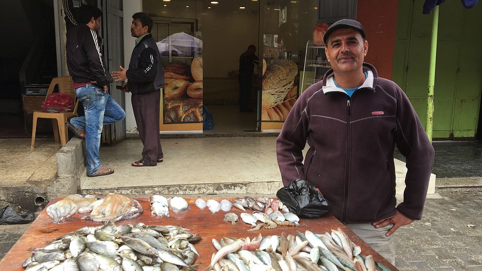 Bild på en palestinsk fiskhandlare som står vid sitt stånd.