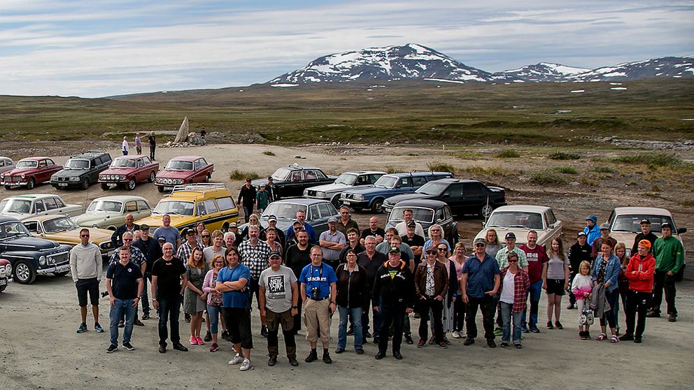 personer framför ett fjäll. Gamla Volvobilar i bakgrunden.