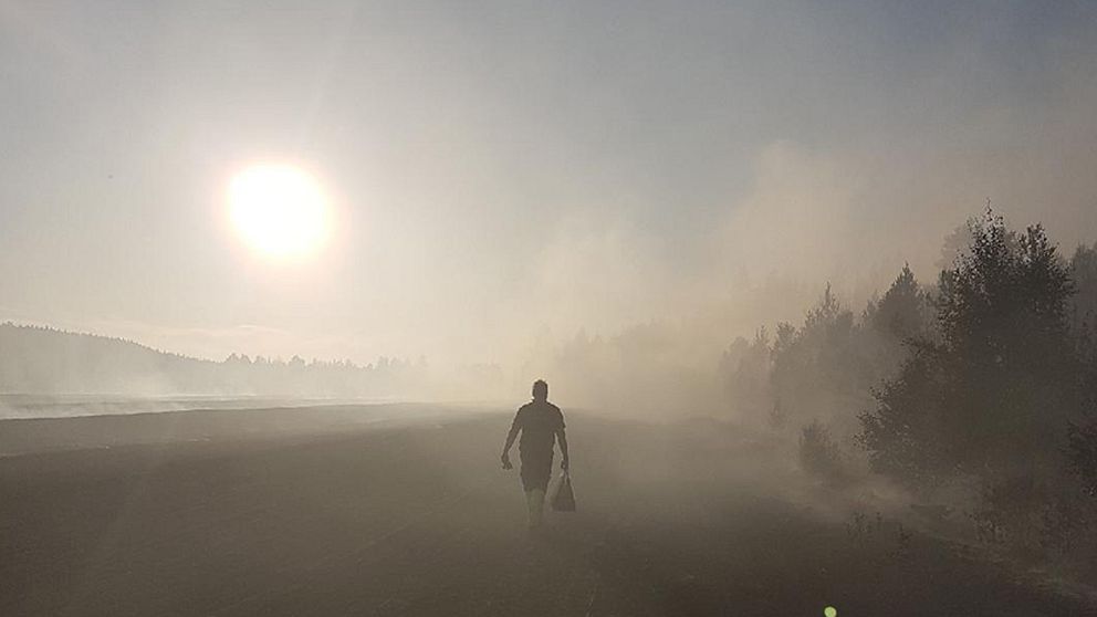 Brandman på väg ut i skogen norr om Helgum – brandrök skymmer solen.