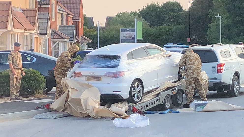 Skyddsklädd polis plastar in den beslagtagna bilen innan de bogserar den därifrån.