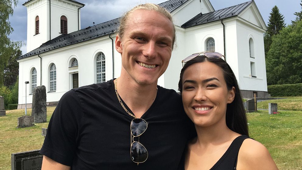 ett ungt, leende par står framför en kyrka