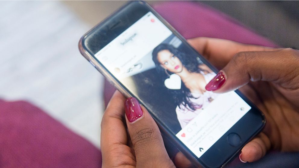Ung kvinna kollar Instagram på mobilen.