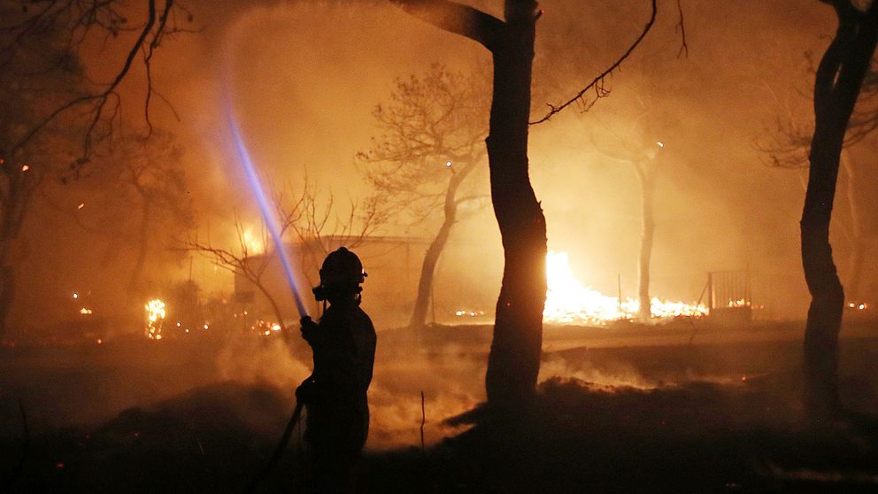 En brandman sprutar vatten på en brand i staden Mati, öster om Aten.