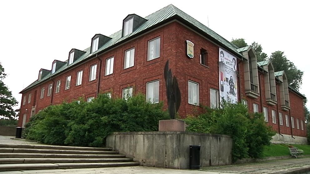 Röd tegelbyggnad med flera våningar och en modern skulptur i förgrunden.
