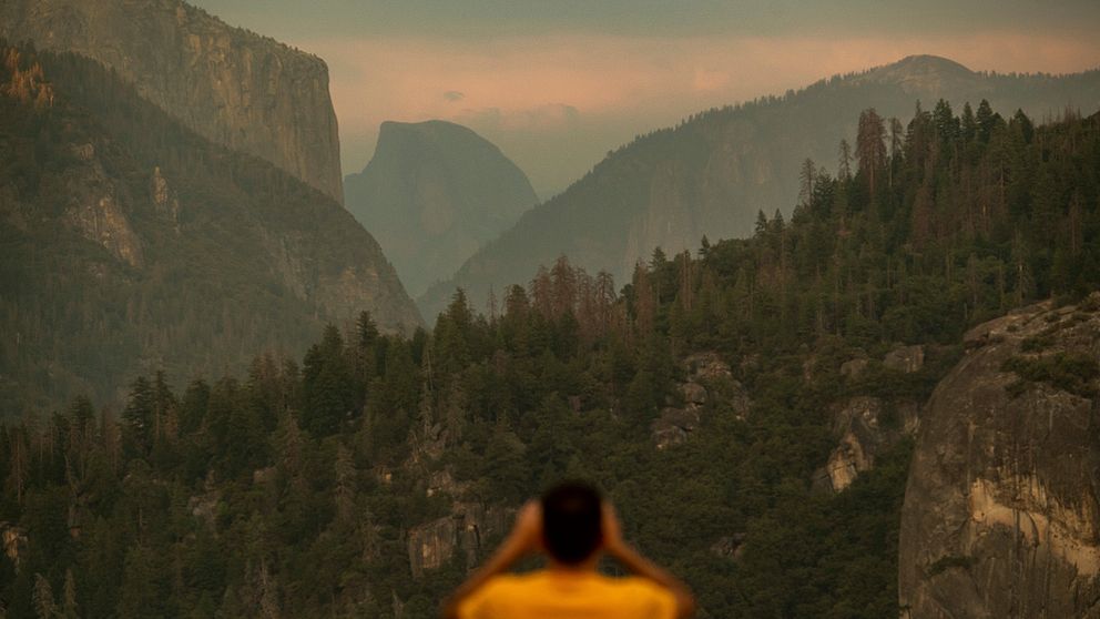 En man tittar ut över nationalparken Yosemite och man ser rök vid bergstopparna.
