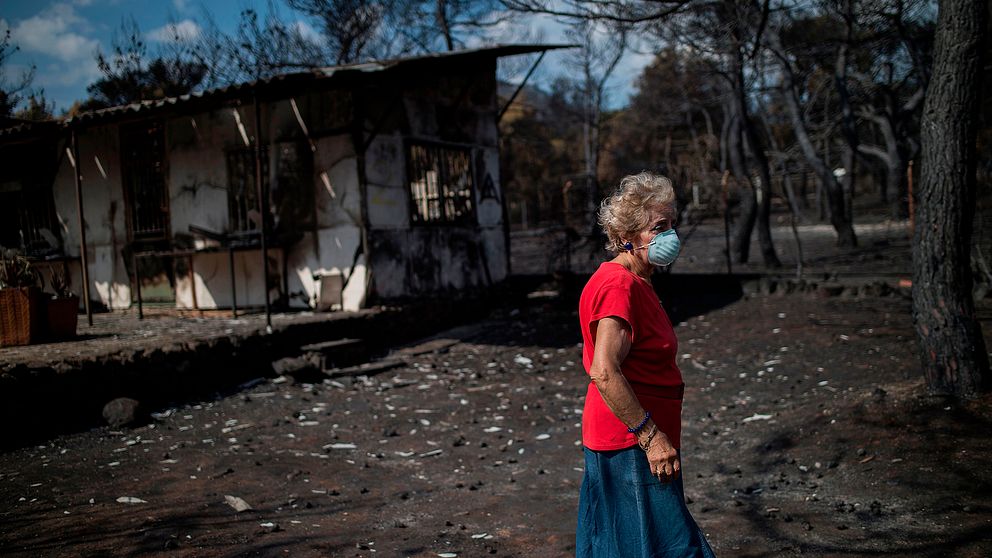 Kvinna i mask utanför nedbänt hus i  byn Neos Voutzas nära Athens