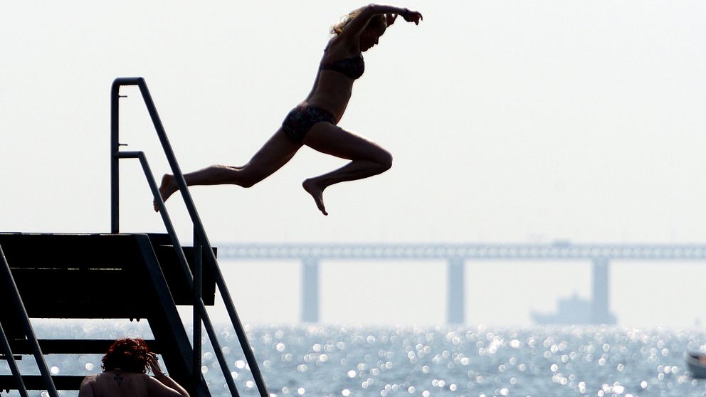 En kvinna hoppar i vattnet vid Västra Hamnen i Malmö med Öresundsbron som bakgrund