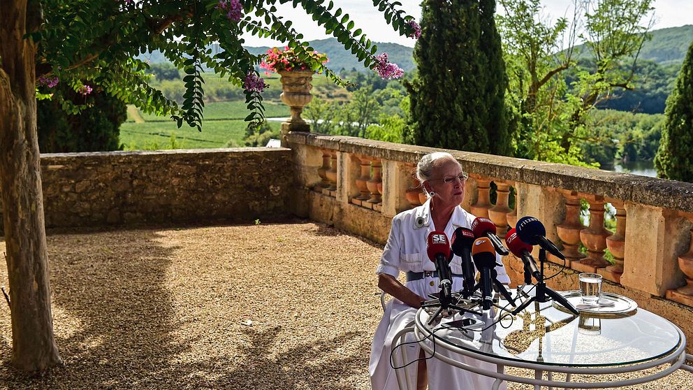 Foto på drottning Margrethe framför ett antal pressmikrofoner i den danska kungafamiljens trädgård.