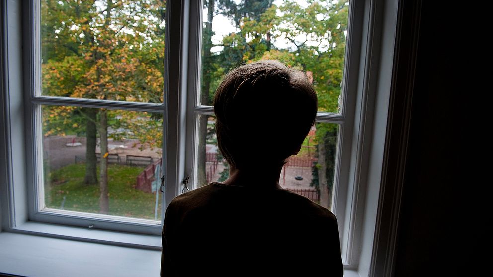 En pojke står och tittar ut genom ett fönster.