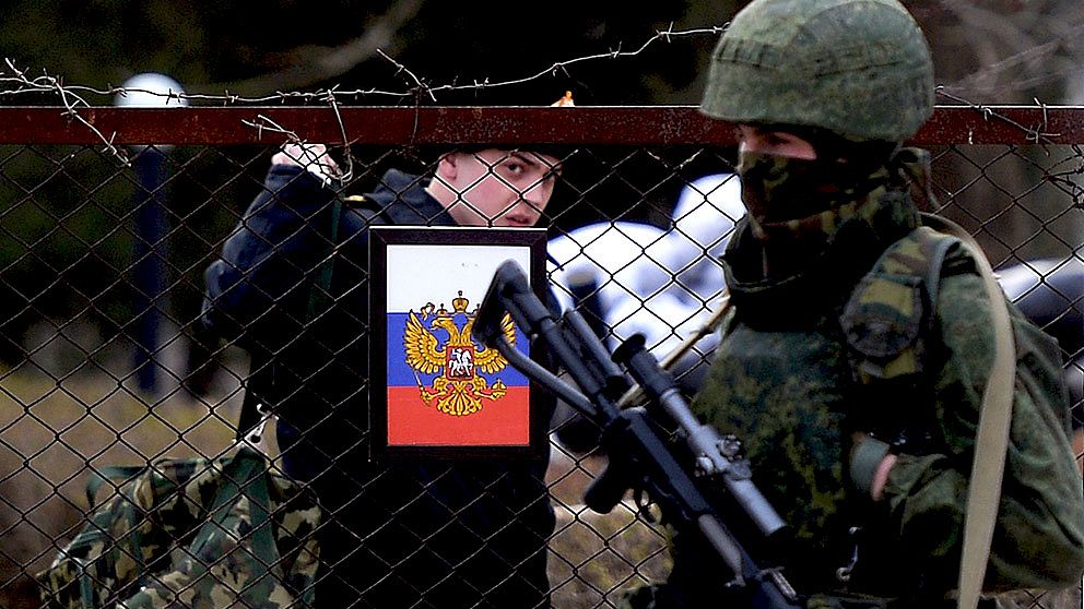 En ukrainsk officer tvingas lämna den ukrainska marinens högkvarter på Krim, under uppsikt av beväpnade proryska ”självförsvarstrupper”.
