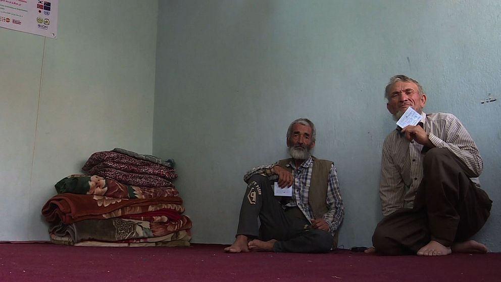 Två afghanska män sitter på golvet intill vikta filtar.