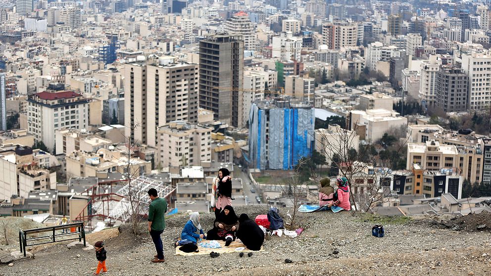 En familj sitter på toppen av en park i Iran som blickar ut över husen.