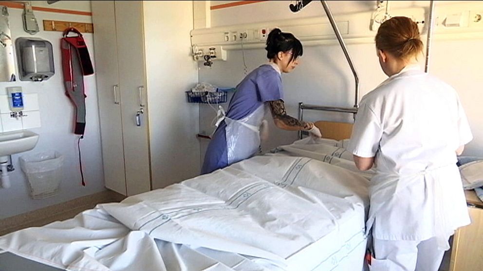 Två kvinnliga undersköterskor hjälps åt att bädda en sjukhus säng