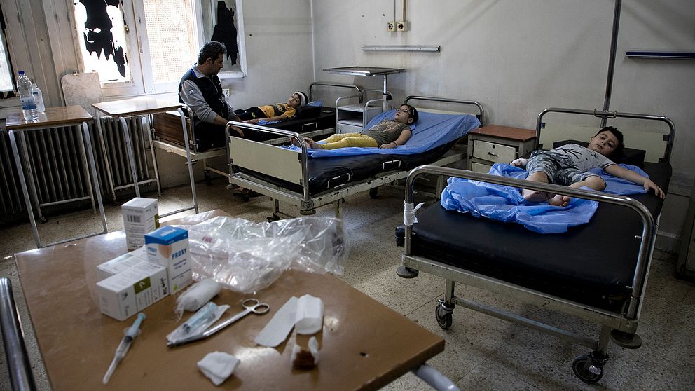 Tre barn ligger på sjukhussängar i Aleppo. En vuxen man vakar över dem.