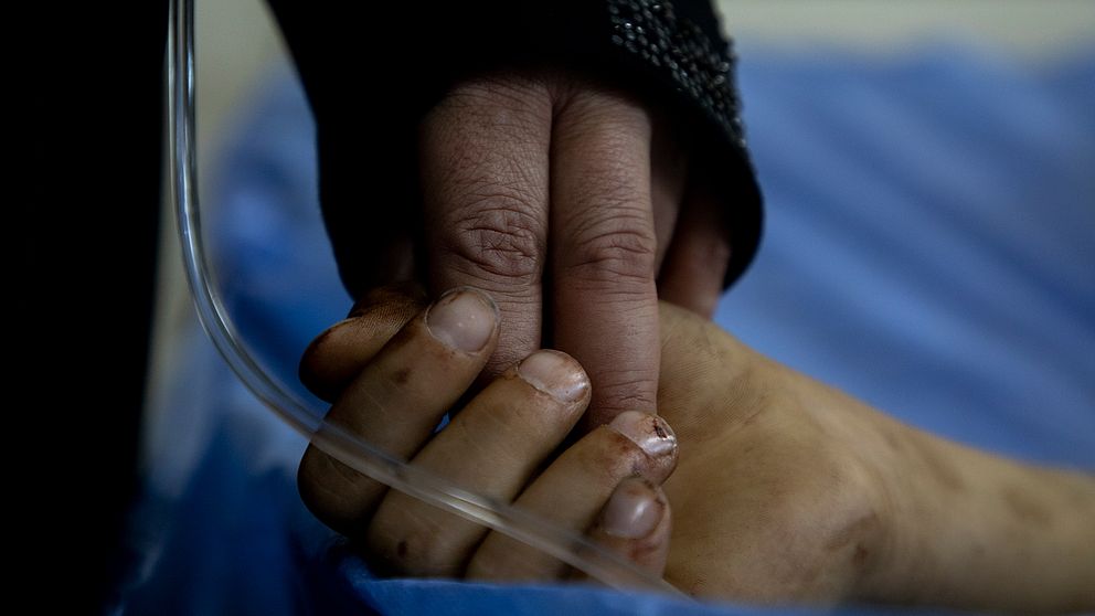 Bild på en mammas hand som håller i sin sjuke sons hand.