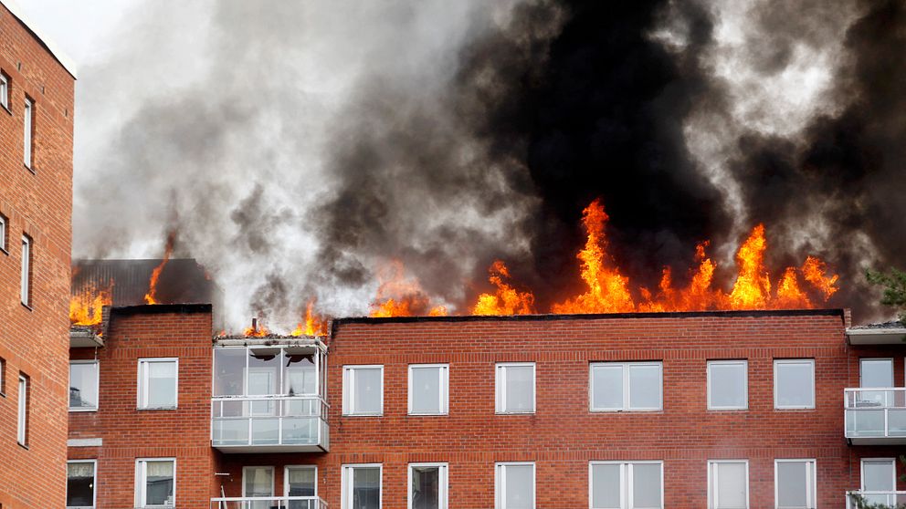 Ett rött tegelhus där stora eldslågor slår ut från taket.