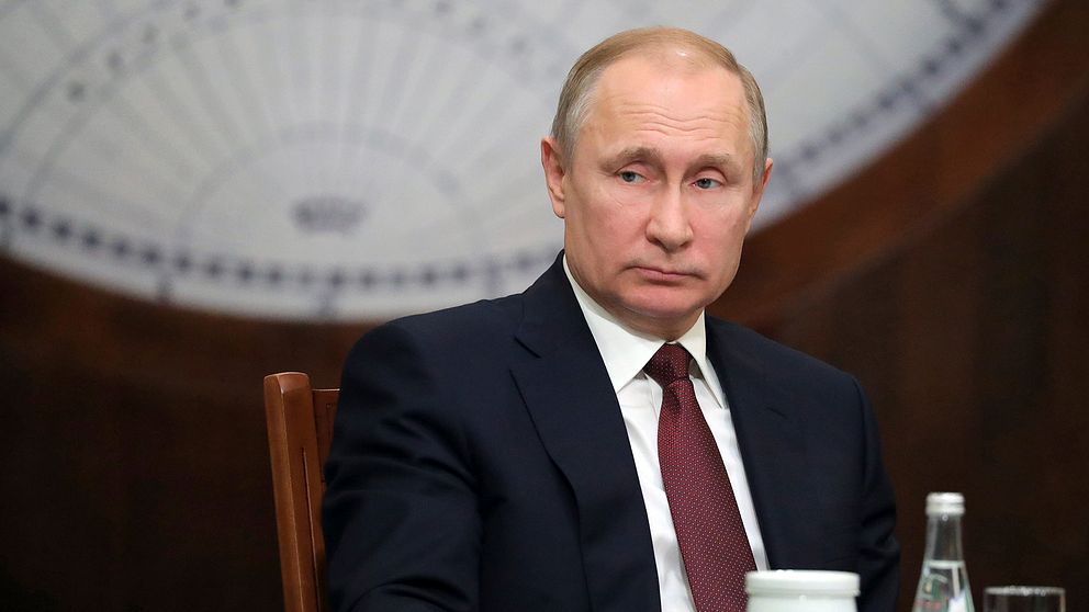 Ryssland president Vladimir Putin i kostym sittandes vid ett bord.