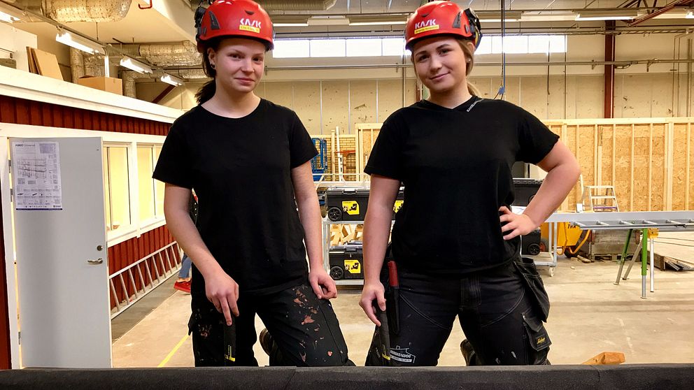 Ellie Klarqvist och Amanda Nordström i svarta byggkläder och röda hjälmar