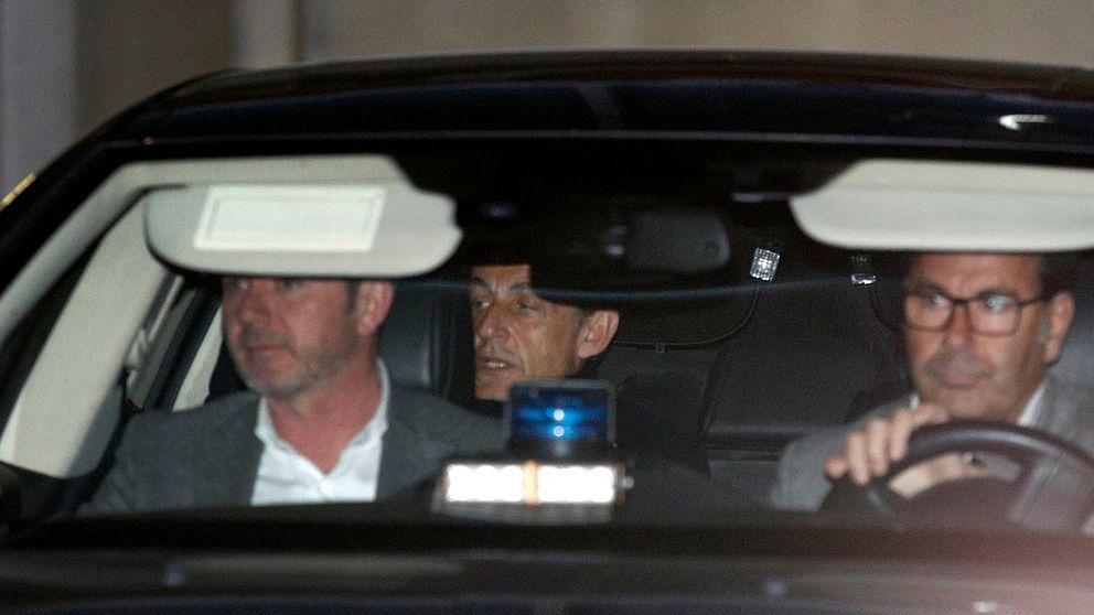 Frankrikes tidigare president Nicolas Sarkozy skymtar i baksätet i en polisbil. Bilden är från i mars i år när han förhördes på en polisstation i Nanterre utanför Paris.