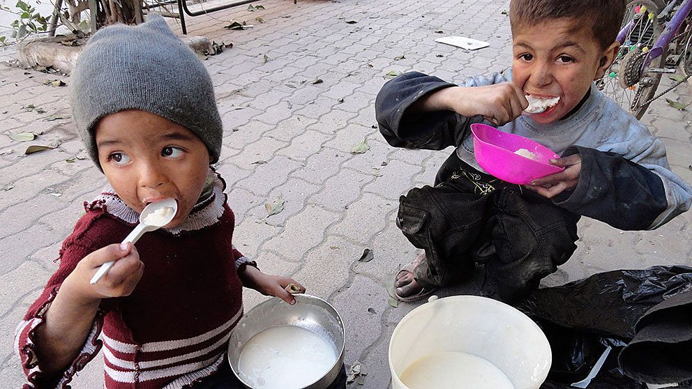 Två barn äter mat som delats ut till dem i flyktinglägret i Yarmouk, Damsaskus.