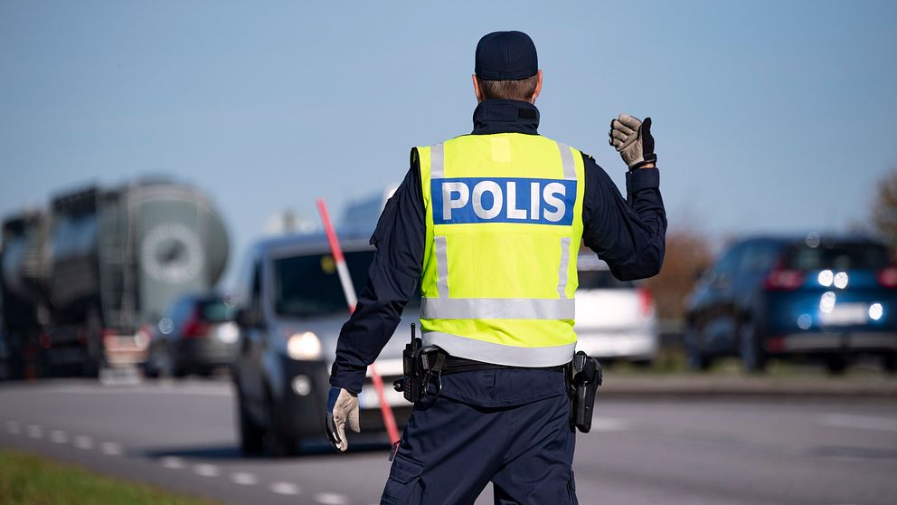 En polis vinkar åt bilar vid en väg.