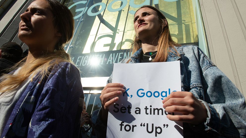 Två kvinnor står framför entrén till Google i New York. En håller upp protestaffisch.