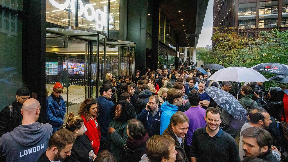 Ett hundratal personer utanför Googles kontor i London. Flera håller i paraplyn.