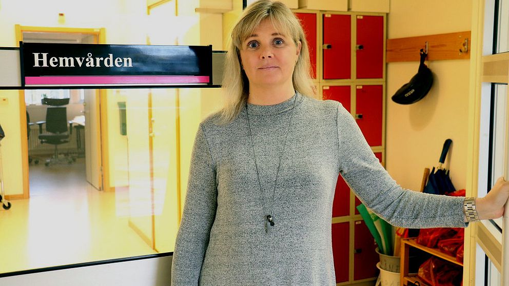 Enhetschefen Maria Möller står vid en dörr med en skylt där det står hemvården på.