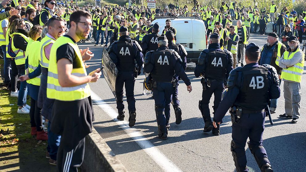 Polis marscherar genom en korsning som blockeras av ”gula västarna”.