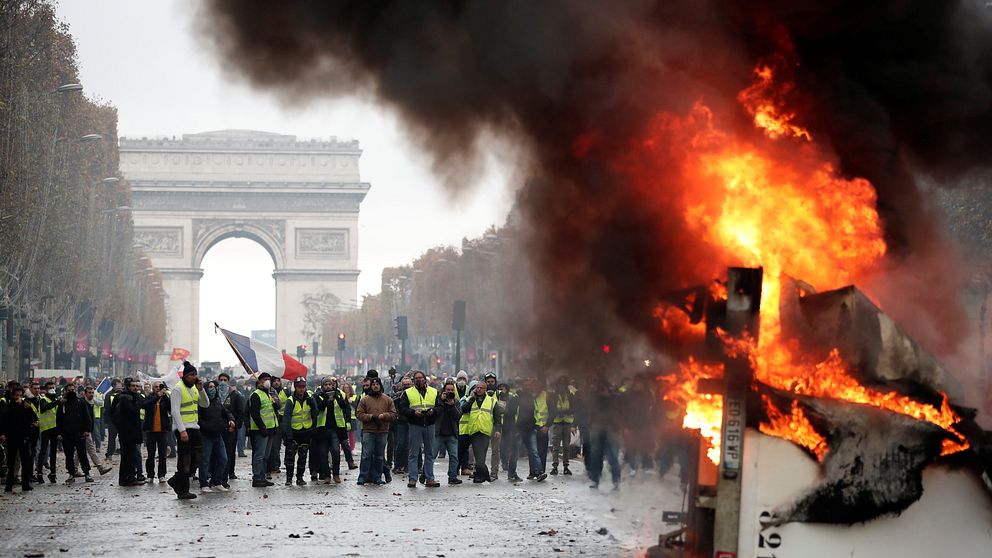 Demonstranter i gula västar protesterar mot Franrikes president Emmanuel Macron. På bilden syns en brinnande lastbil och triumfbågen.