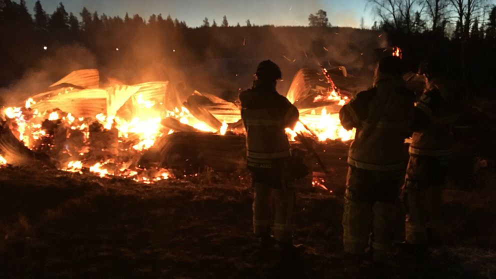 två brandmän syns i silhuett mot brinnade rester av byggnad